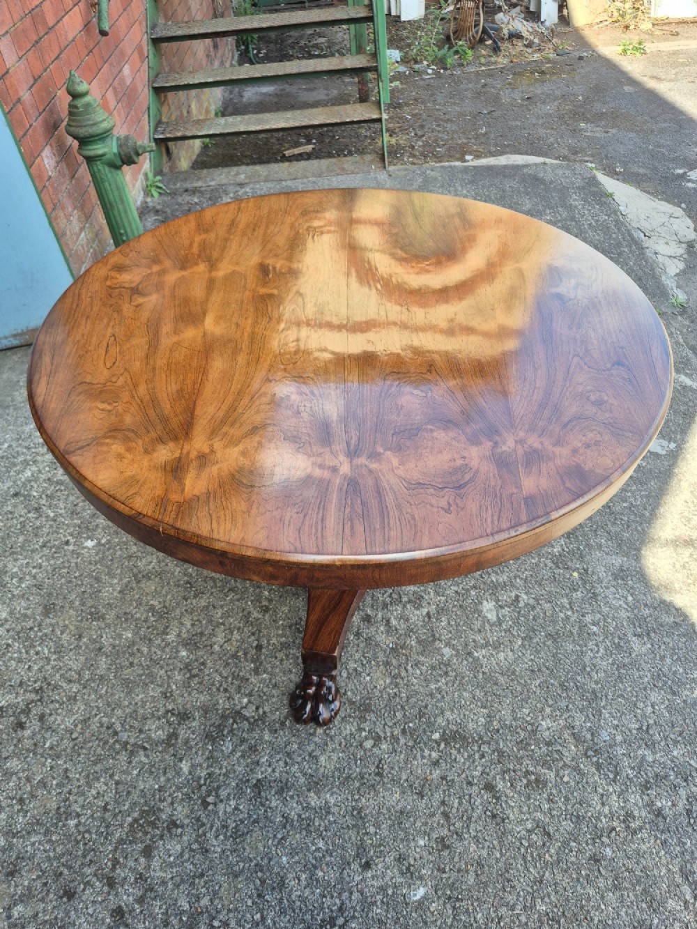 A circular Regency rosewood breakfast table featuring a figured veneer top resting on a central pedestal column with a triform base and carved feet. View XI
