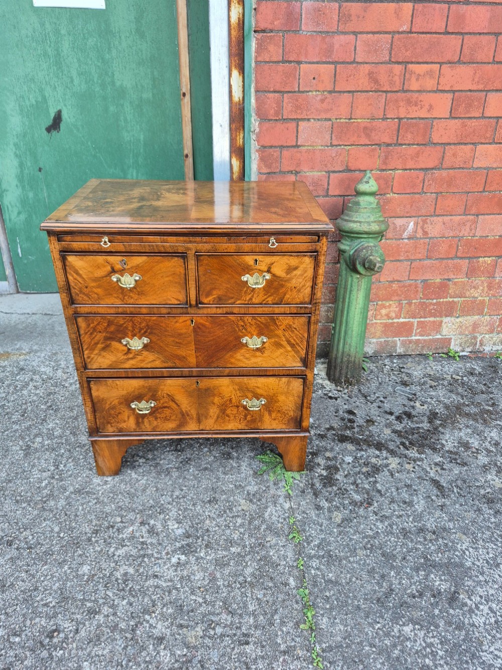 A small burr walnut bachelors chest featuring four drawers with brass handles, a brushing slide, and bracket feet.
