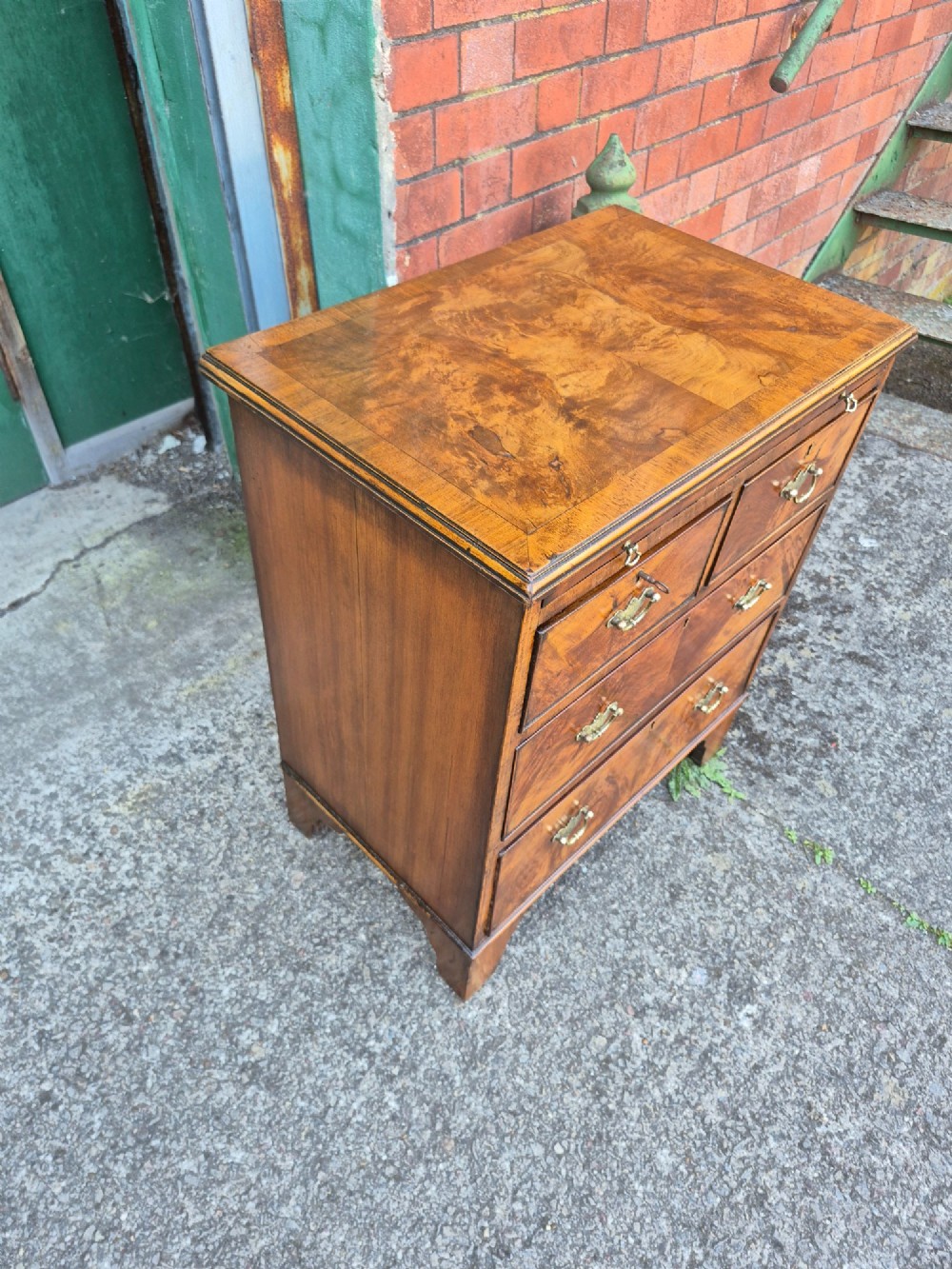 A small burr walnut bachelors chest featuring four drawers with brass handles, a brushing slide, and bracket feet. View IV
