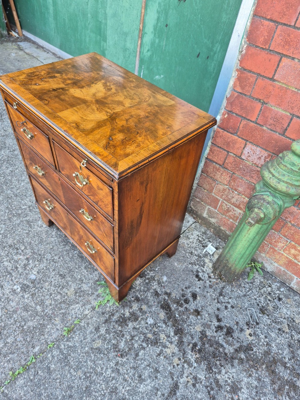 A small burr walnut bachelors chest featuring four drawers with brass handles, a brushing slide, and bracket feet. View V