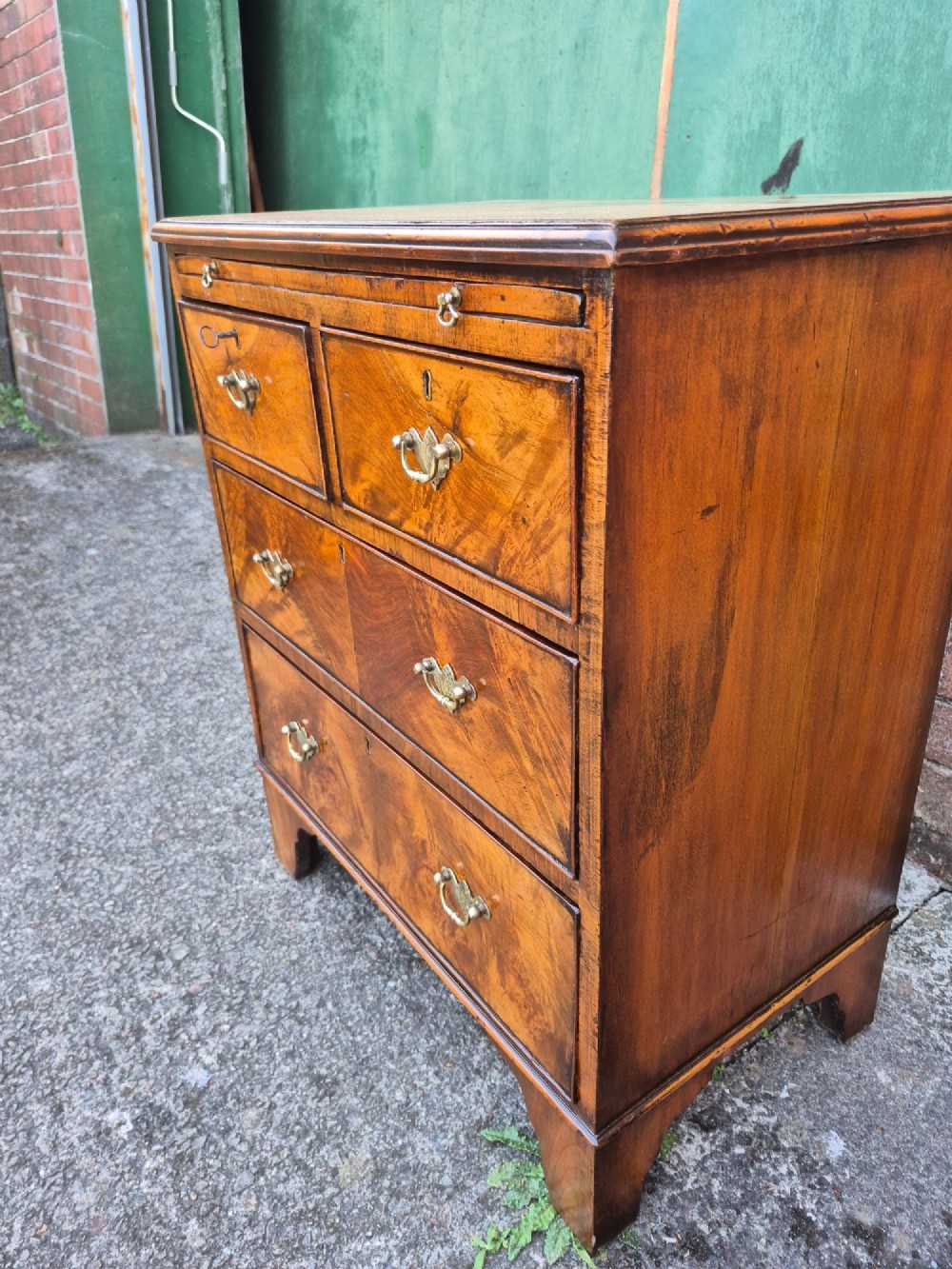 A small burr walnut bachelors chest featuring four drawers with brass handles, a brushing slide, and bracket feet. View VII
