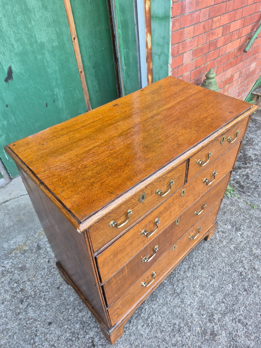 A George II golden oak chest of drawers featuring two short drawers over three long graduated drawers with brass swan-neck handles and bracket feet. View VI