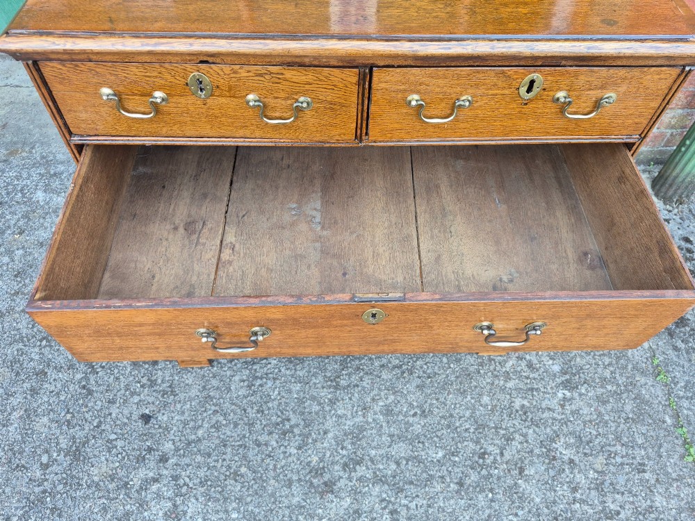 A George II golden oak chest of drawers featuring two short drawers over three long graduated drawers with brass swan-neck handles and bracket feet. View VII