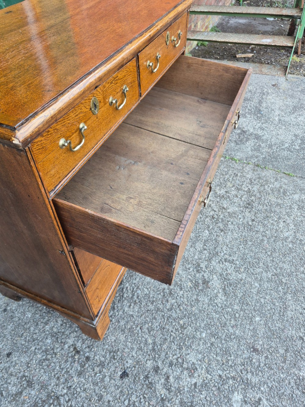 A George II golden oak chest of drawers featuring two short drawers over three long graduated drawers with brass swan-neck handles and bracket feet. View VIII