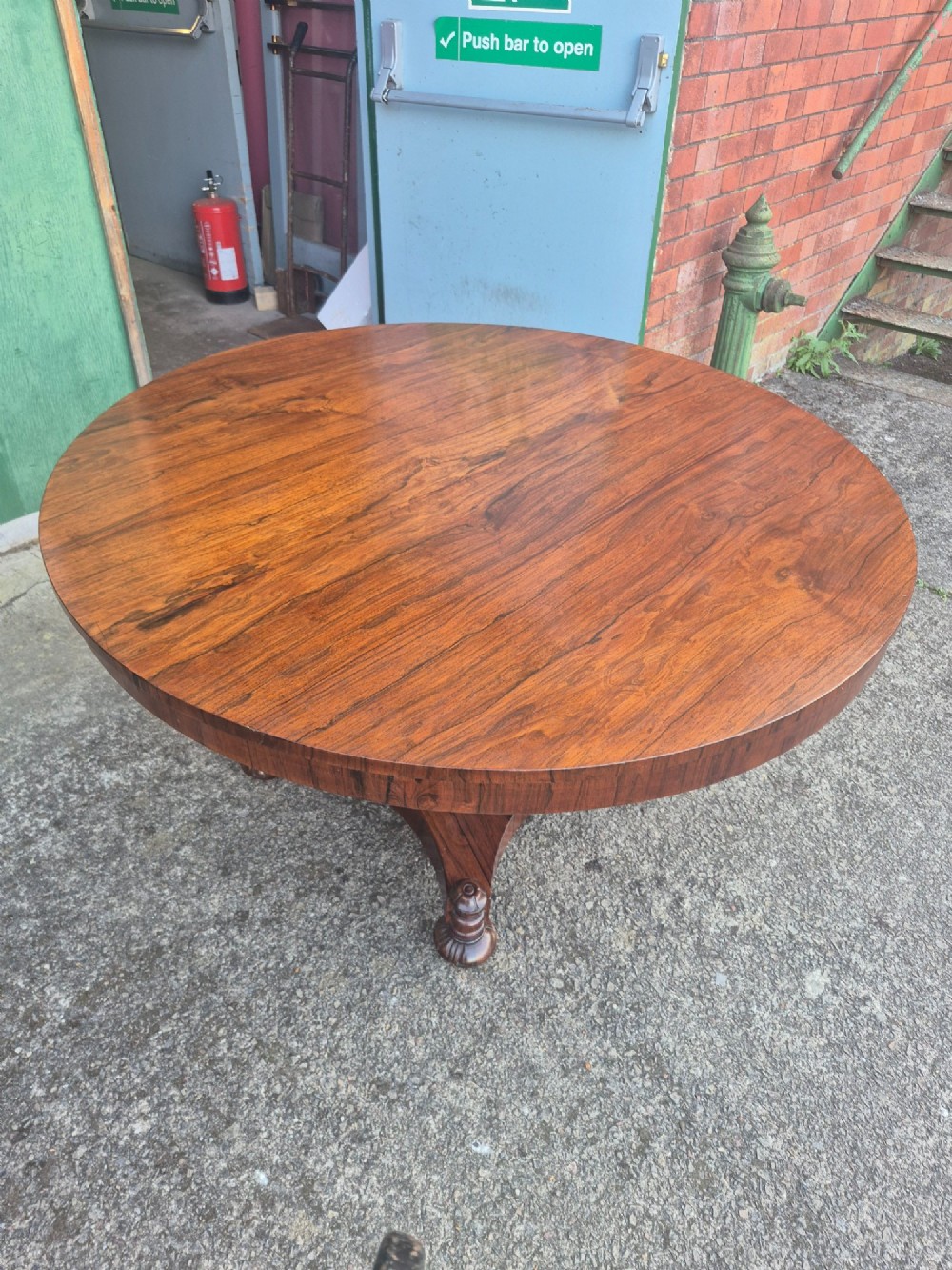 A circular Regency rosewood breakfast table featuring a figured veneer top, carved acanthus leaf pedestal column, and a concaved quadform base. View II