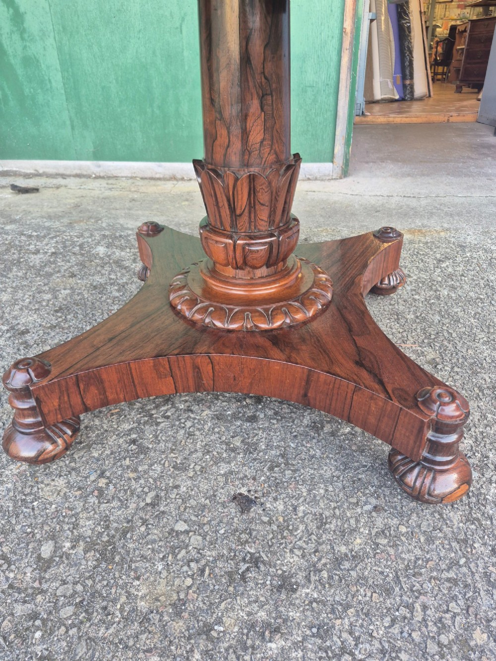 A circular Regency rosewood breakfast table featuring a figured veneer top, carved acanthus leaf pedestal column, and a concaved quadform base. View V