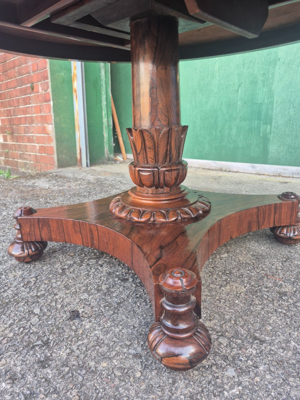 A circular Regency rosewood breakfast table featuring a figured veneer top, carved acanthus leaf pedestal column, and a concaved quadform base. View VI