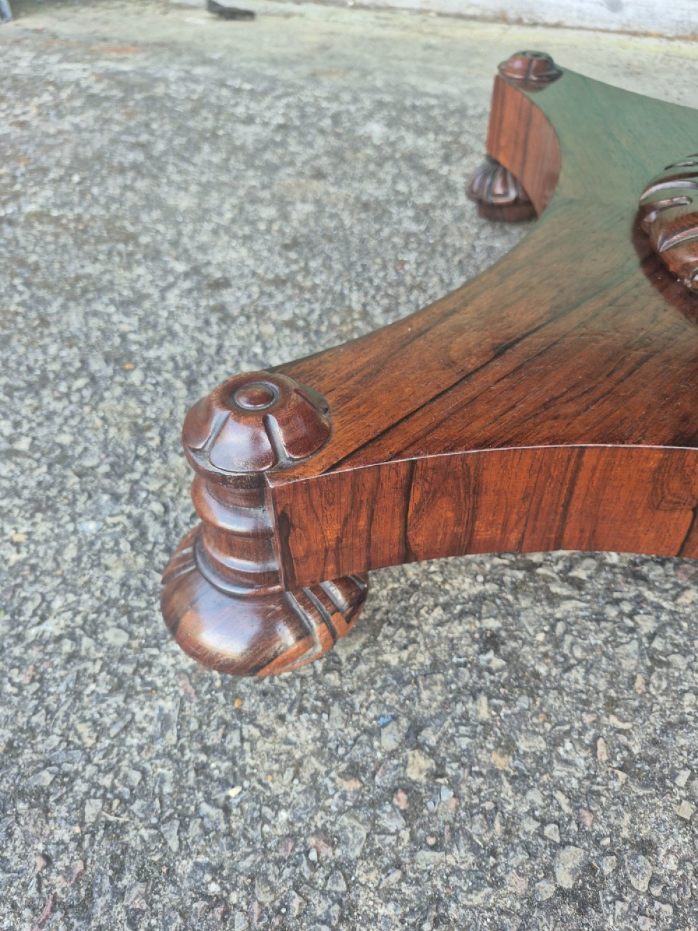 A circular Regency rosewood breakfast table featuring a figured veneer top, carved acanthus leaf pedestal column, and a concaved quadform base. View VII