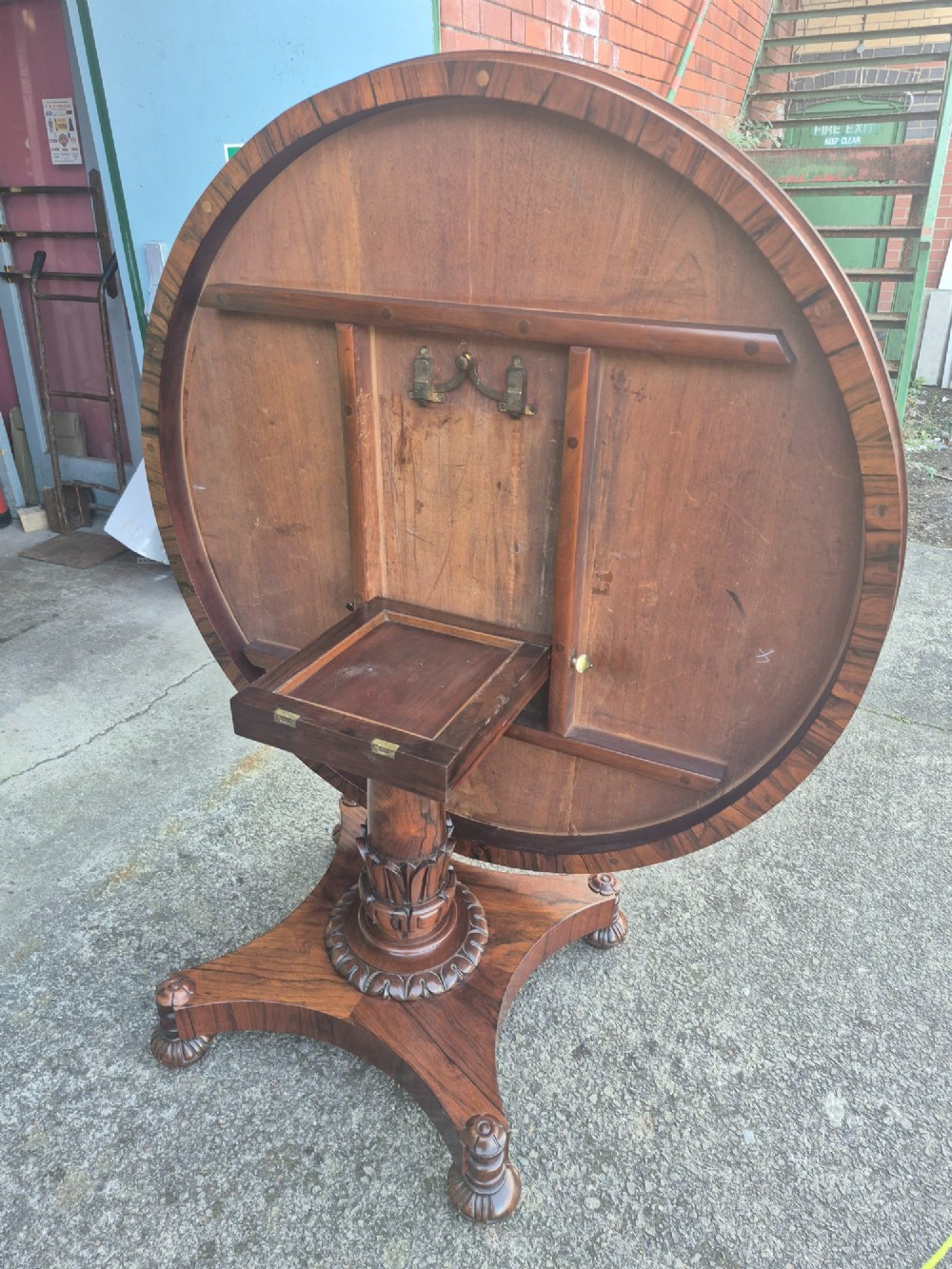 A circular Regency rosewood breakfast table featuring a figured veneer top, carved acanthus leaf pedestal column, and a concaved quadform base. View IX