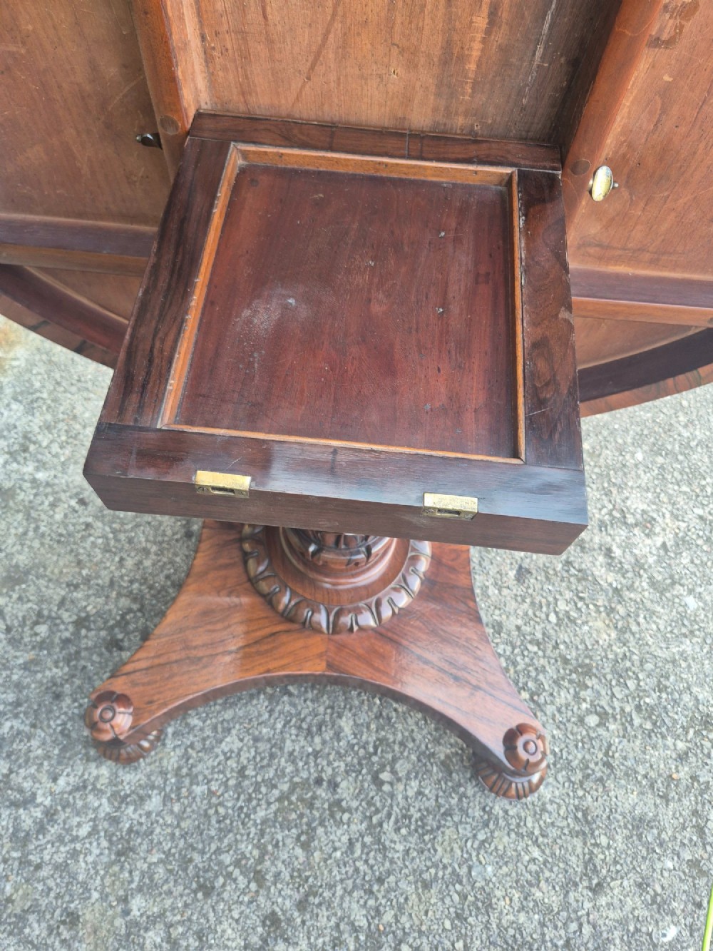 A circular Regency rosewood breakfast table featuring a figured veneer top, carved acanthus leaf pedestal column, and a concaved quadform base. View X