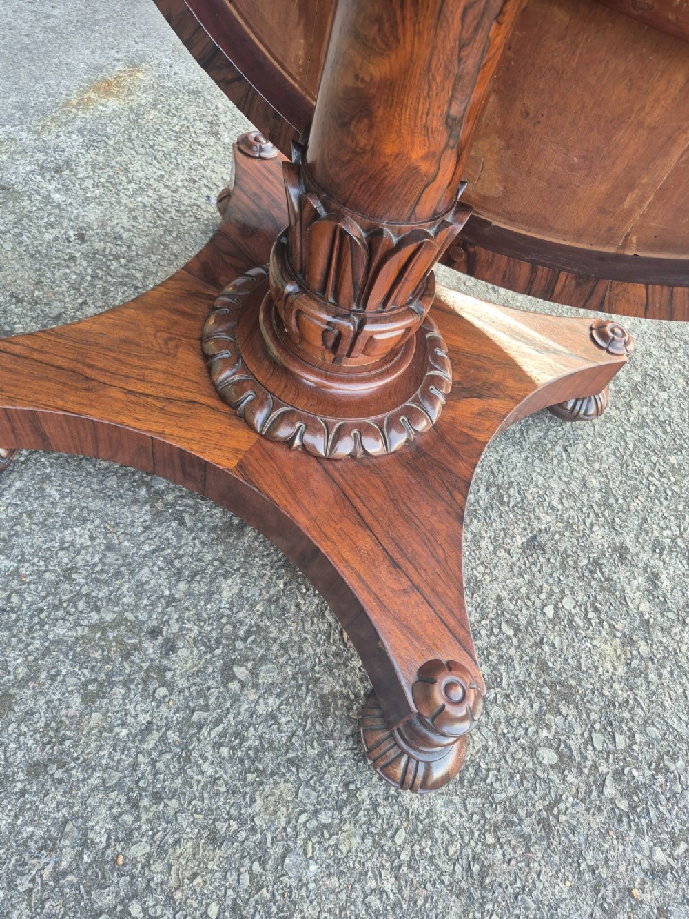 A circular Regency rosewood breakfast table featuring a figured veneer top, carved acanthus leaf pedestal column, and a concaved quadform base. View XI