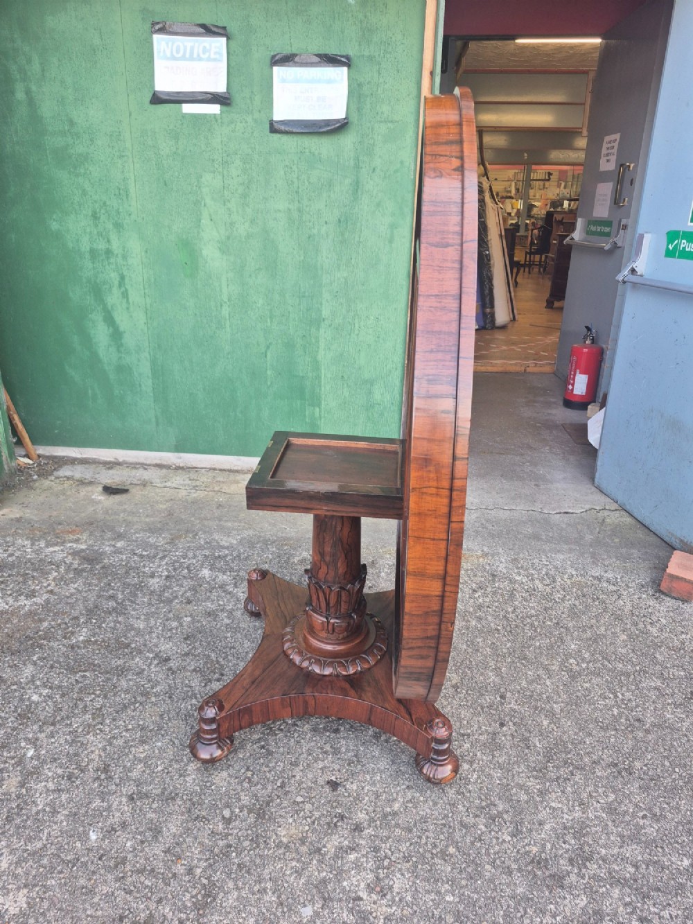 A circular Regency rosewood breakfast table featuring a figured veneer top, carved acanthus leaf pedestal column, and a concaved quadform base. View XII