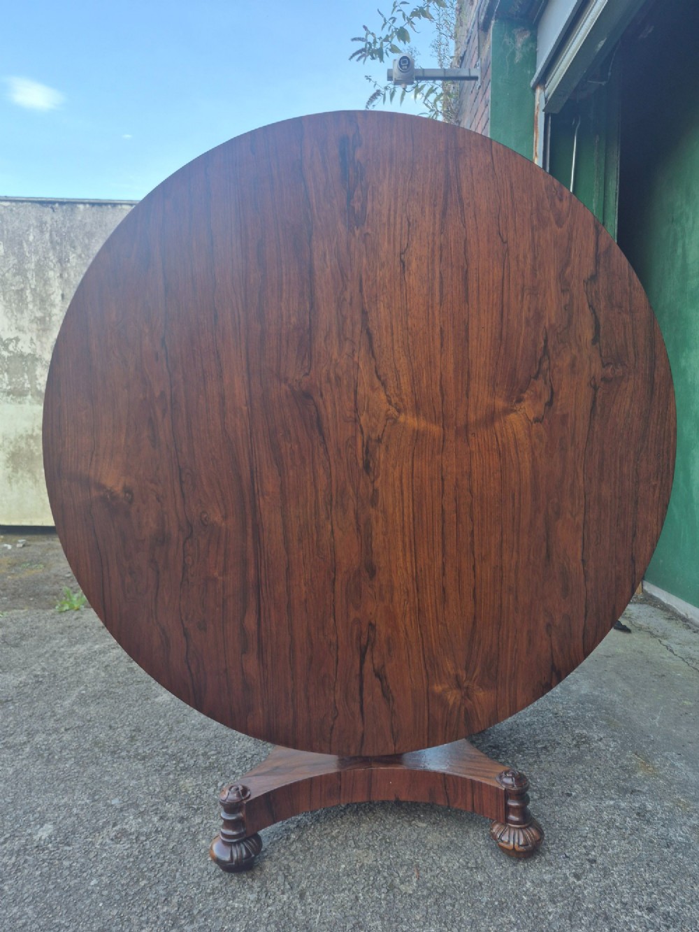 A circular Regency rosewood breakfast table featuring a figured veneer top, carved acanthus leaf pedestal column, and a concaved quadform base. View XIII