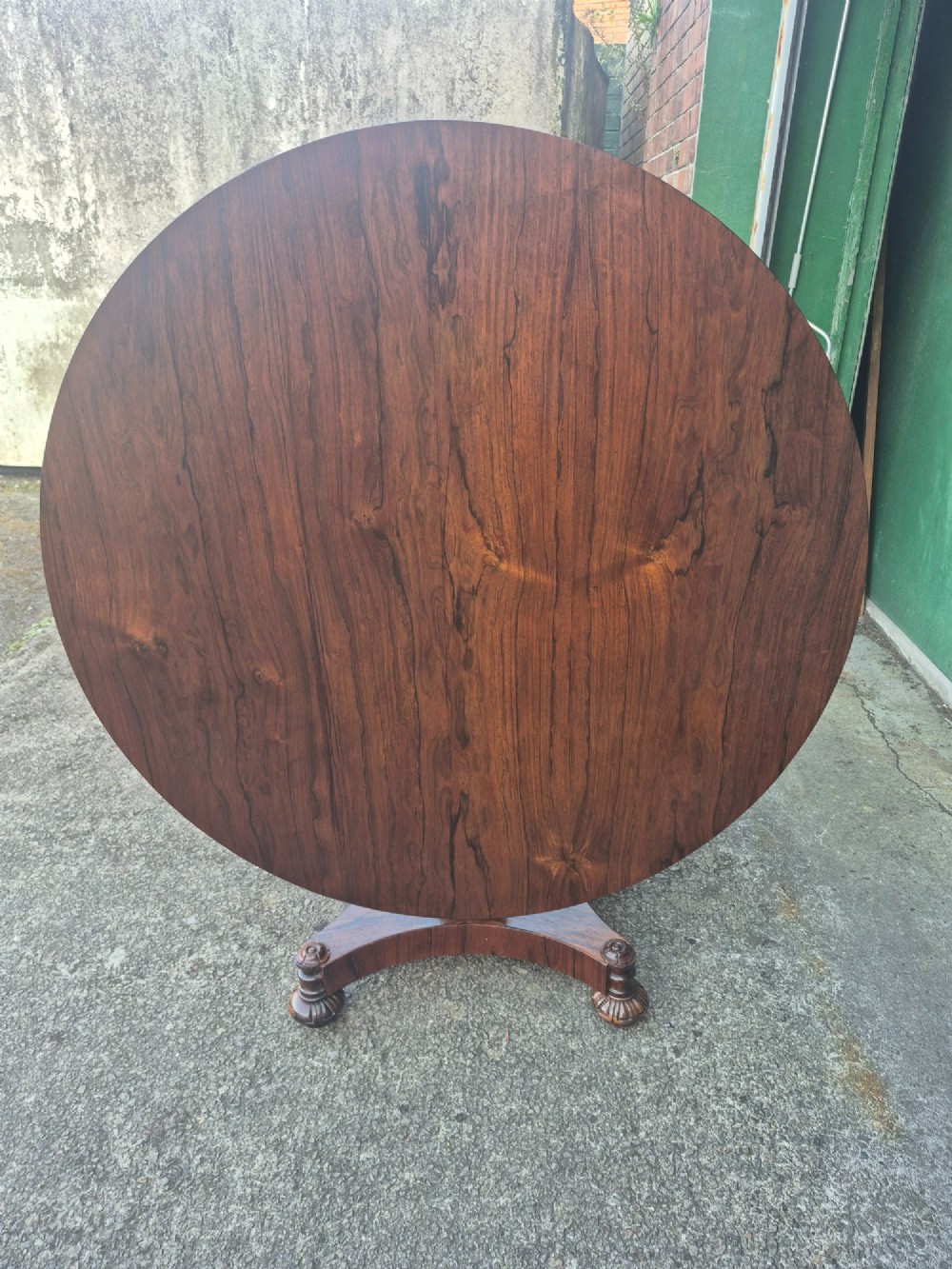 A circular Regency rosewood breakfast table featuring a figured veneer top, carved acanthus leaf pedestal column, and a concaved quadform base. View XIV