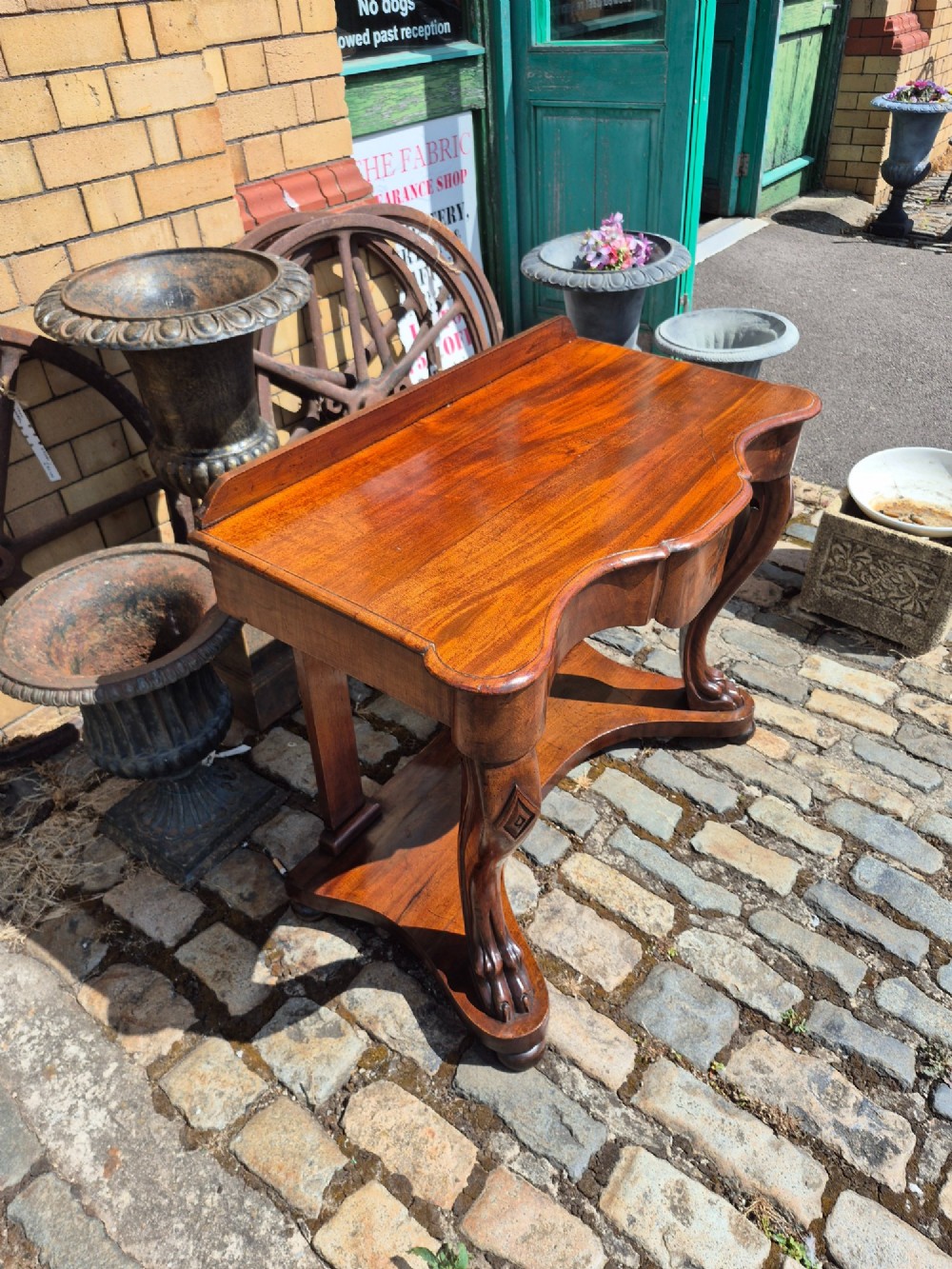 An early Victorian mahogany console table with a shaped serpentine top, carved cabriole front legs, and an undertier shelf resting on a plinth base. View II