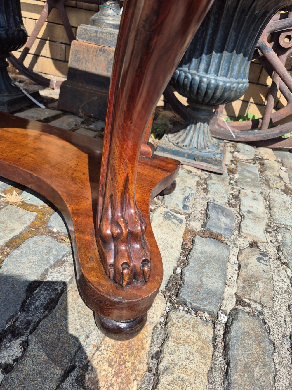 An early Victorian mahogany console table with a shaped serpentine top, carved cabriole front legs, and an undertier shelf resting on a plinth base. View IV