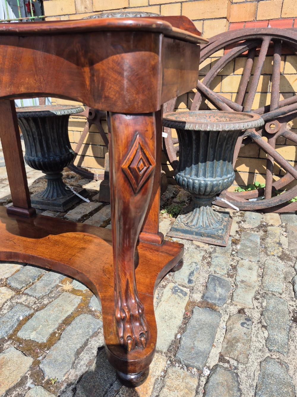 An early Victorian mahogany console table with a shaped serpentine top, carved cabriole front legs, and an undertier shelf resting on a plinth base. View V