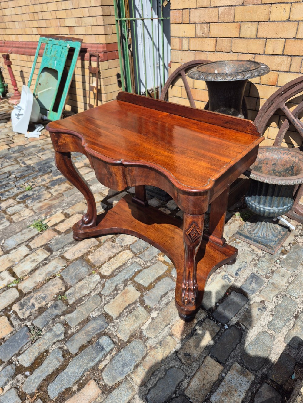 An early Victorian mahogany console table with a shaped serpentine top, carved cabriole front legs, and an undertier shelf resting on a plinth base. View VIII