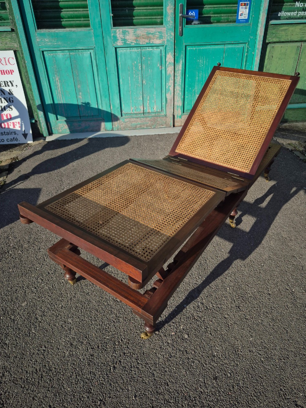 An antique campaign-style daybed crafted from dark timber with three woven cane panels, adjustable reclining sections, turned legs, and brass castors. View II