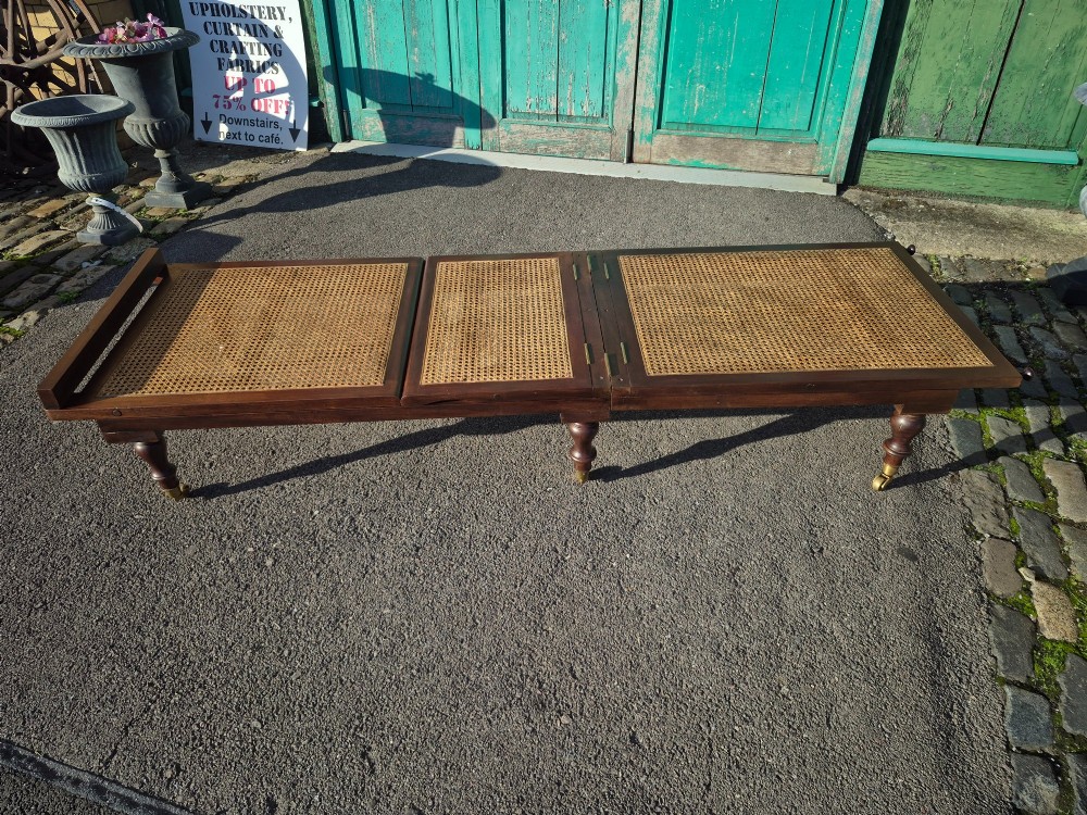 An antique campaign-style daybed crafted from dark timber with three woven cane panels, adjustable reclining sections, turned legs, and brass castors. View III