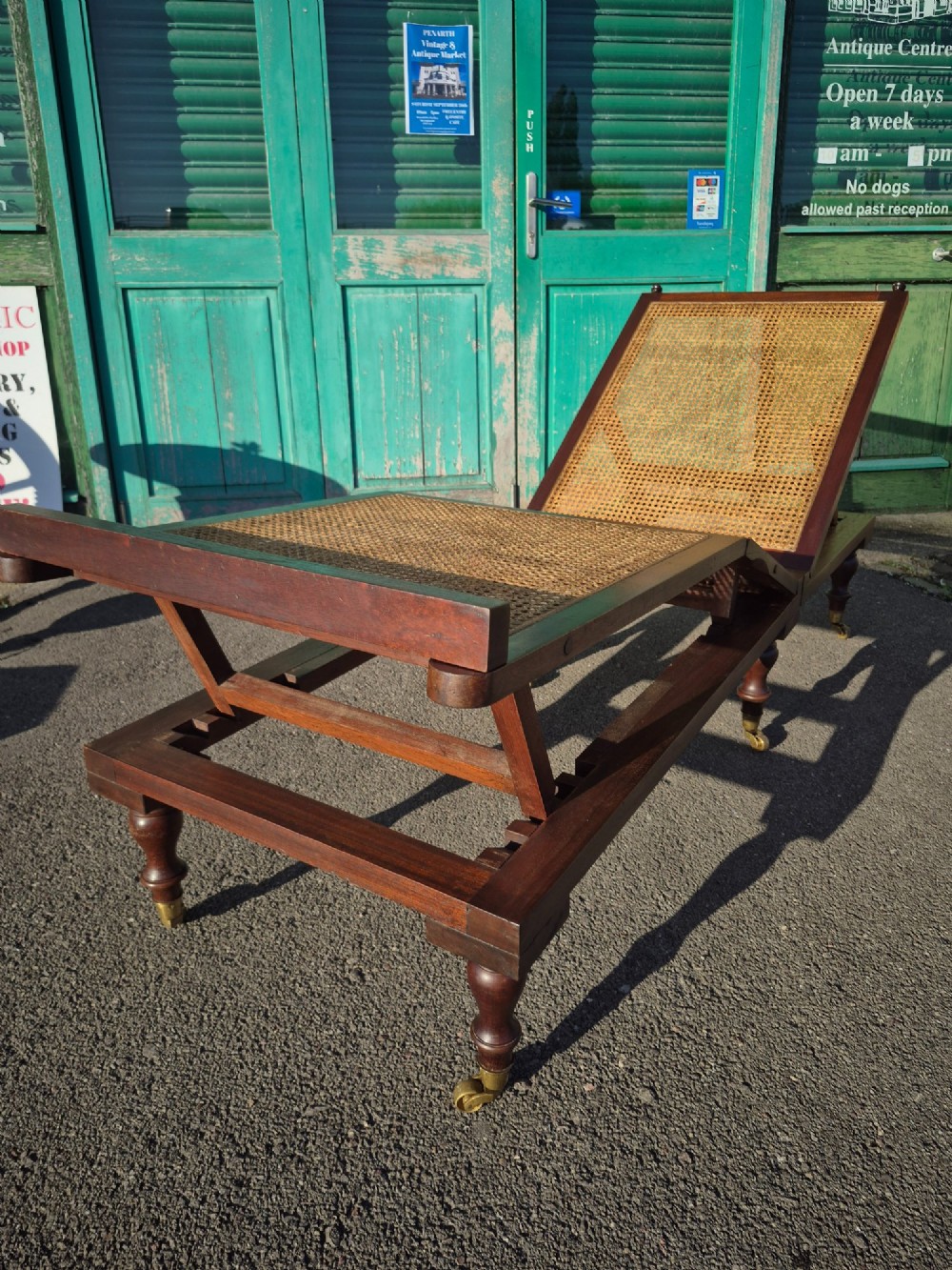 An antique campaign-style daybed crafted from dark timber with three woven cane panels, adjustable reclining sections, turned legs, and brass castors. View IV