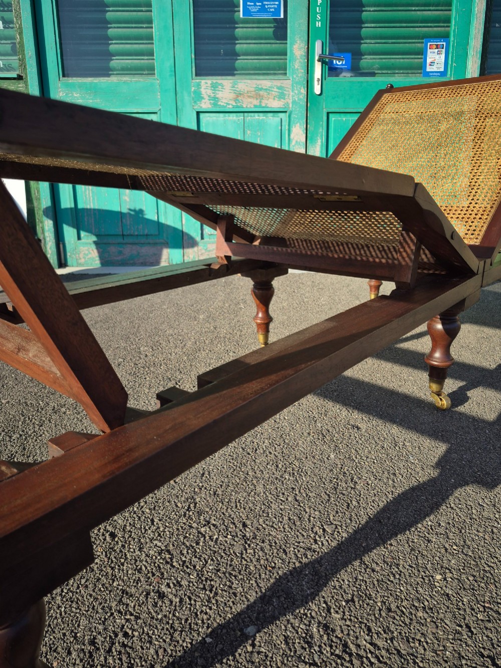 An antique campaign-style daybed crafted from dark timber with three woven cane panels, adjustable reclining sections, turned legs, and brass castors. View VII