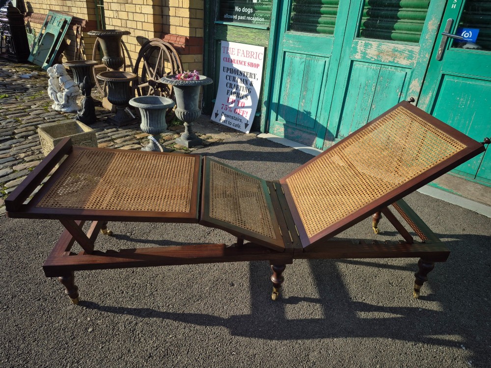 An antique campaign-style daybed crafted from dark timber with three woven cane panels, adjustable reclining sections, turned legs, and brass castors. View X