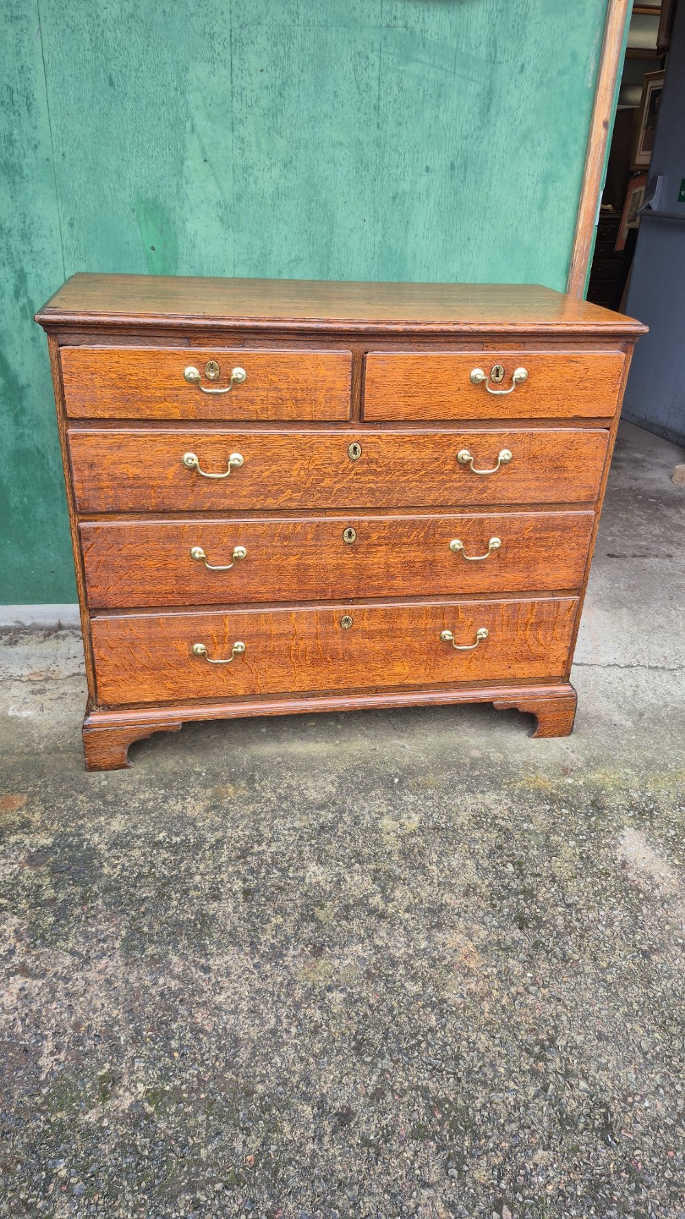 A Georgian golden oak chest of drawers featuring a two over three drawer arrangement with brass swan-neck handles and bracket feet.