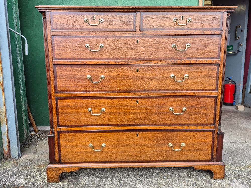A golden oak Georgian chest of drawers featuring two short drawers over three long drawers with brass handles, reeded side columns, and bracket feet. View II