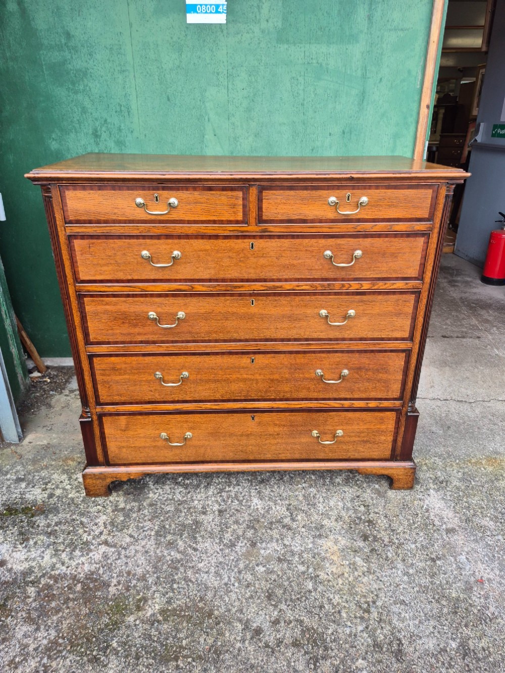 A golden oak Georgian chest of drawers featuring two short drawers over three long drawers with brass handles, reeded side columns, and bracket feet. View III