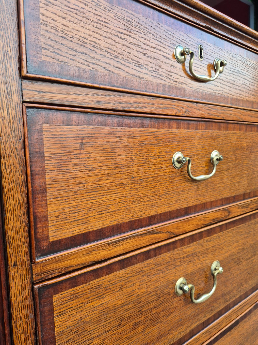 A golden oak Georgian chest of drawers featuring two short drawers over three long drawers with brass handles, reeded side columns, and bracket feet. View V