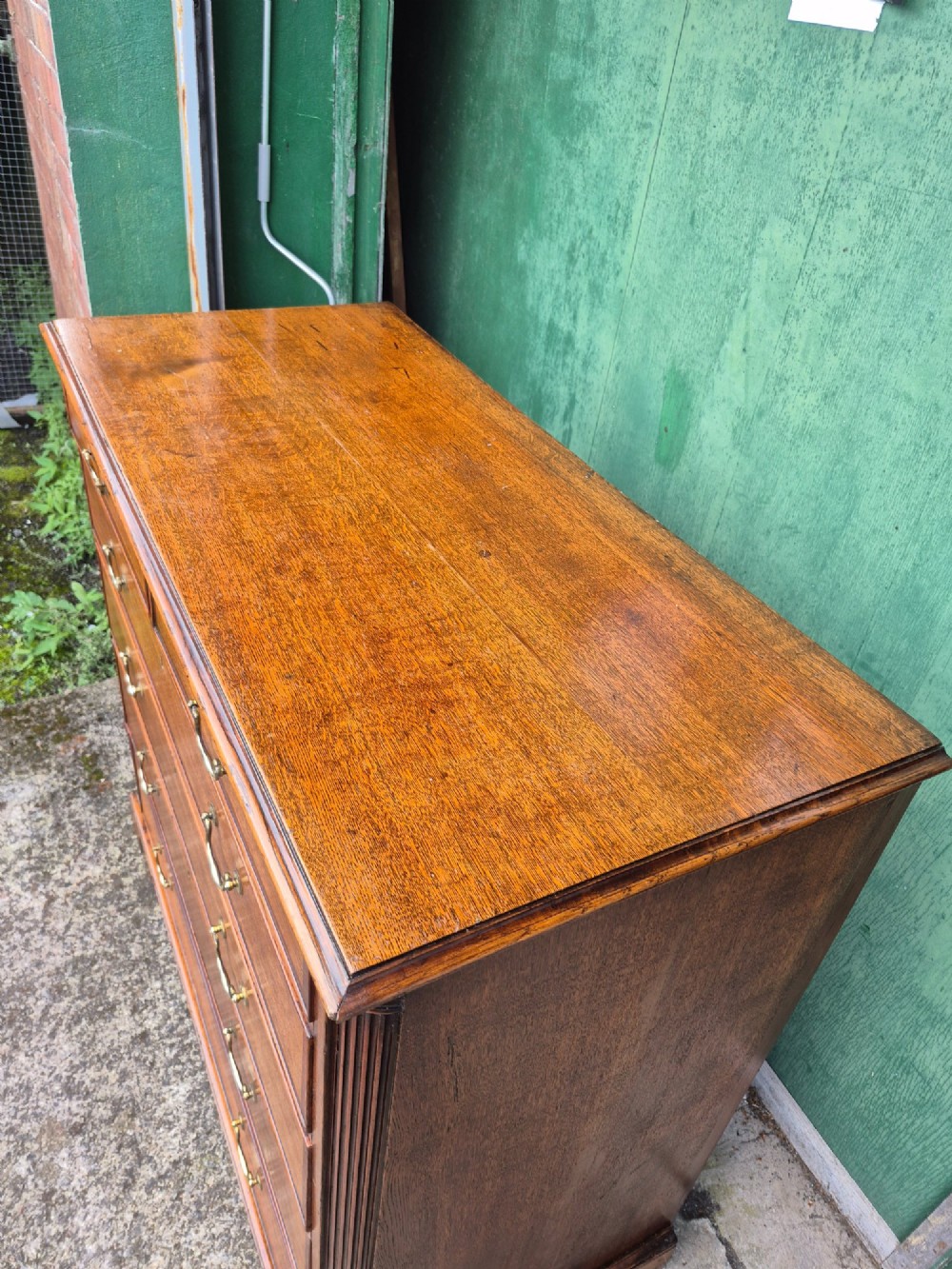 A golden oak Georgian chest of drawers featuring two short drawers over three long drawers with brass handles, reeded side columns, and bracket feet. View VII
