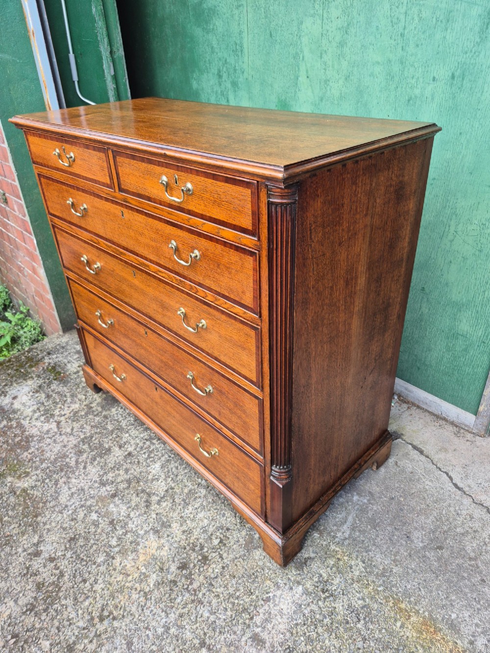 A golden oak Georgian chest of drawers featuring two short drawers over three long drawers with brass handles, reeded side columns, and bracket feet. View VIII