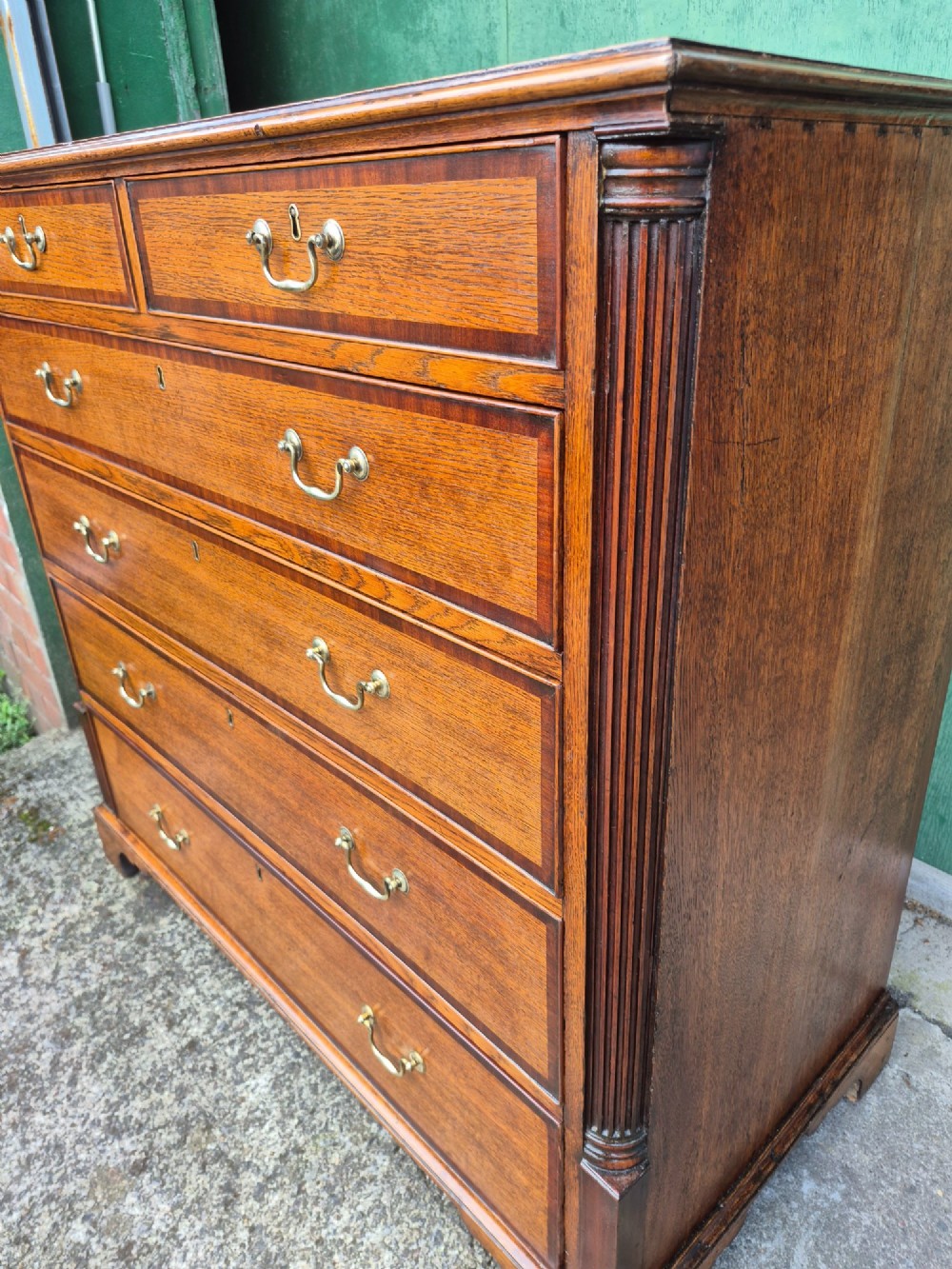 A golden oak Georgian chest of drawers featuring two short drawers over three long drawers with brass handles, reeded side columns, and bracket feet. View X