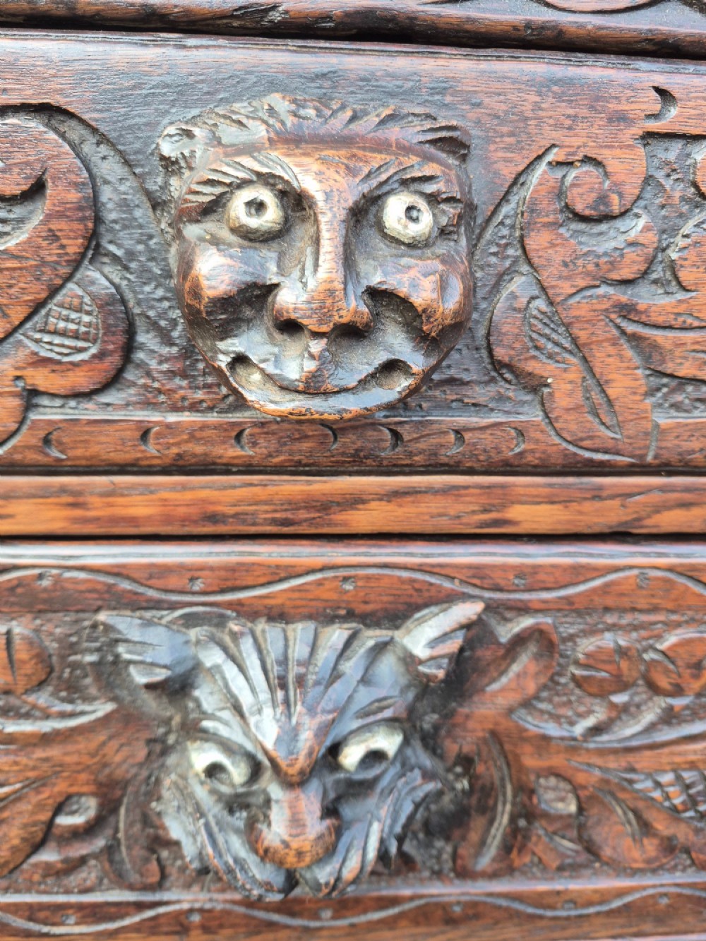 A nineteenth-century dark oak chest of drawers featuring hand-carved grotesque Green Man face masks and elaborate foliate scrollwork across the front. View III