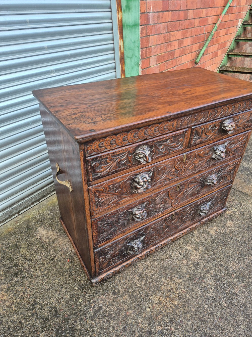 A nineteenth-century dark oak chest of drawers featuring hand-carved grotesque Green Man face masks and elaborate foliate scrollwork across the front. View VII