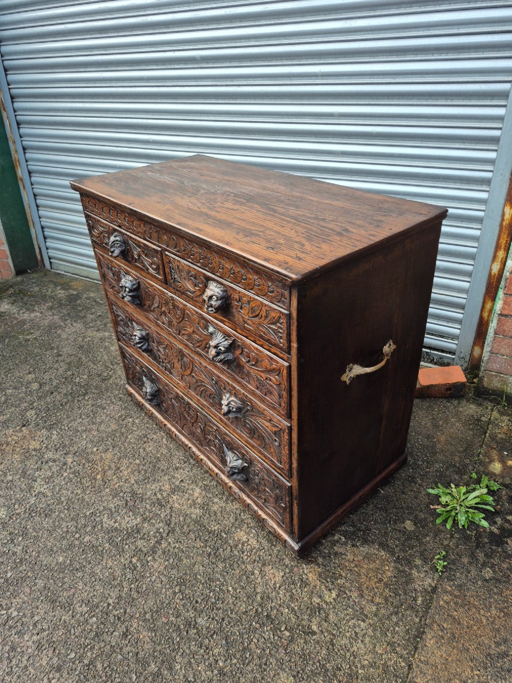 A nineteenth-century dark oak chest of drawers featuring hand-carved grotesque Green Man face masks and elaborate foliate scrollwork across the front. View VIII