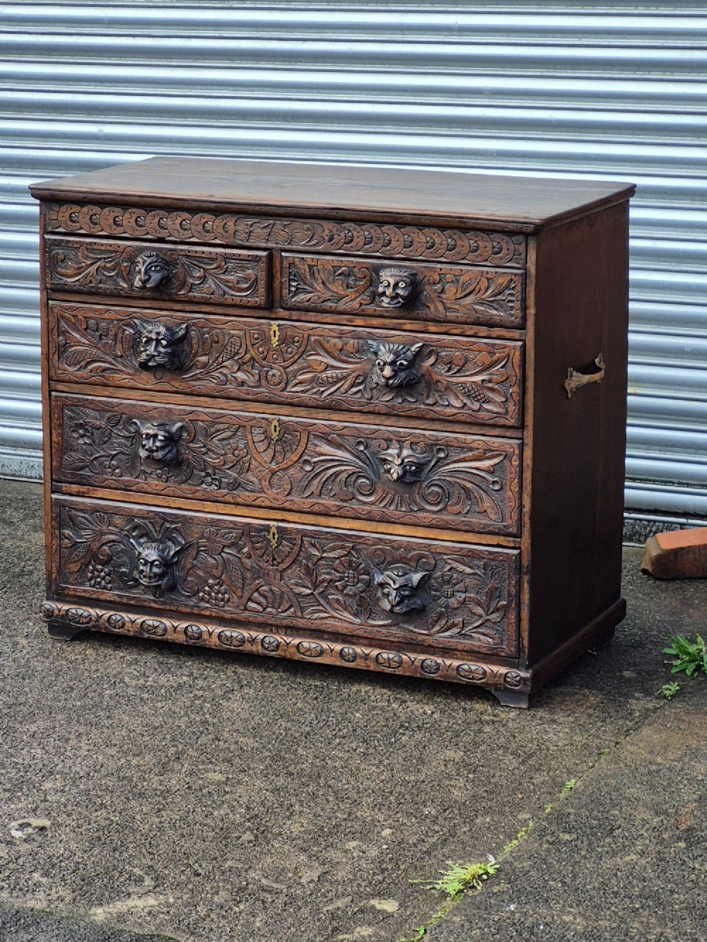 A nineteenth-century dark oak chest of drawers featuring hand-carved grotesque Green Man face masks and elaborate foliate scrollwork across the front. View XI