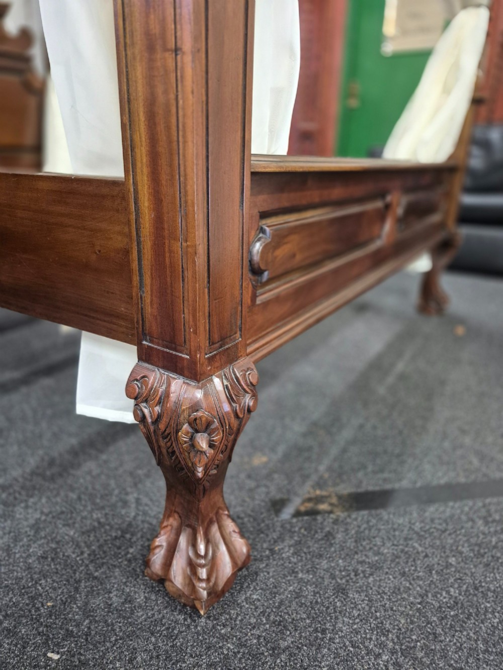 A dark hardwood queen-size four-poster bed frame featuring turned posts, a detailed carved headboard, and draped cream fabric. View V