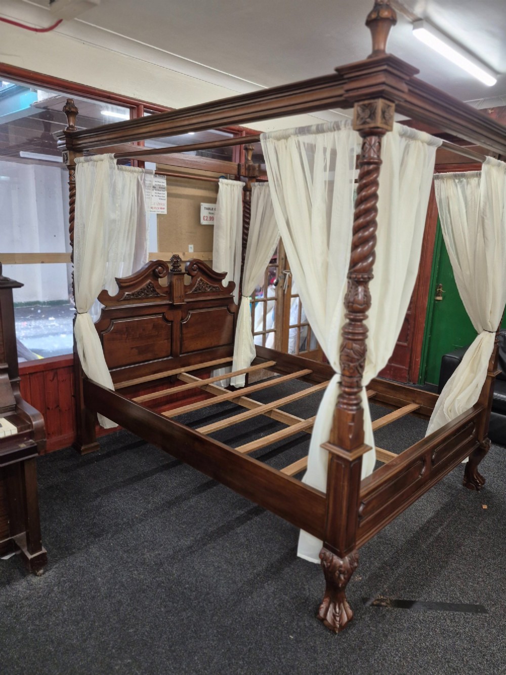 A dark hardwood queen-size four-poster bed frame featuring turned posts, a detailed carved headboard, and draped cream fabric. View VI