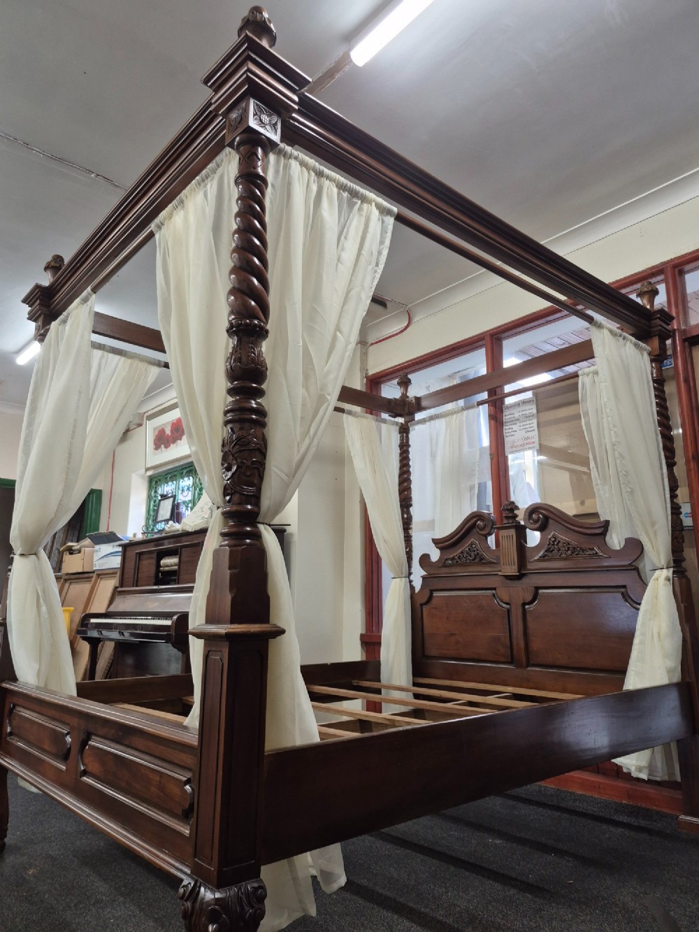 A dark hardwood queen-size four-poster bed frame featuring turned posts, a detailed carved headboard, and draped cream fabric. View VIII