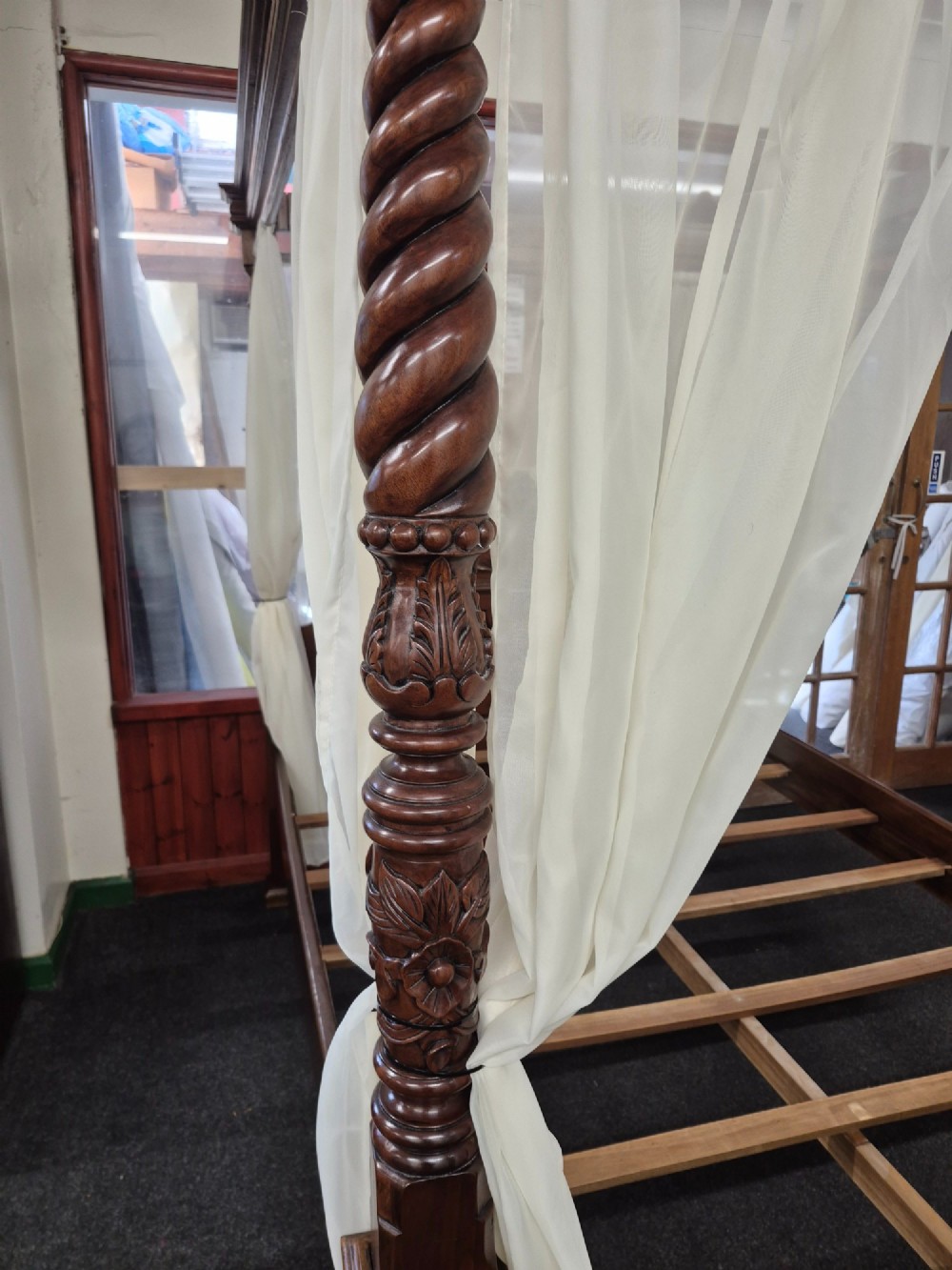 A dark hardwood queen-size four-poster bed frame featuring turned posts, a detailed carved headboard, and draped cream fabric. View IX