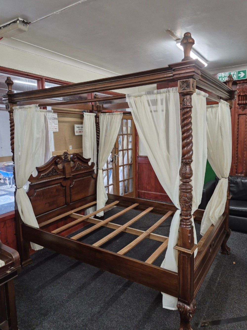 A dark hardwood queen-size four-poster bed frame featuring turned posts, a detailed carved headboard, and draped cream fabric. View XI