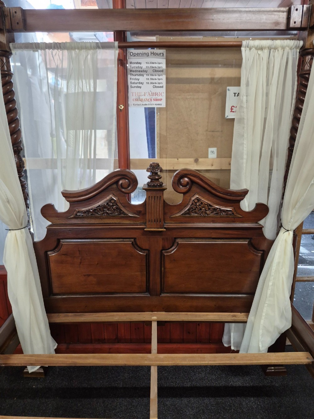 A dark hardwood queen-size four-poster bed frame featuring turned posts, a detailed carved headboard, and draped cream fabric. View XII
