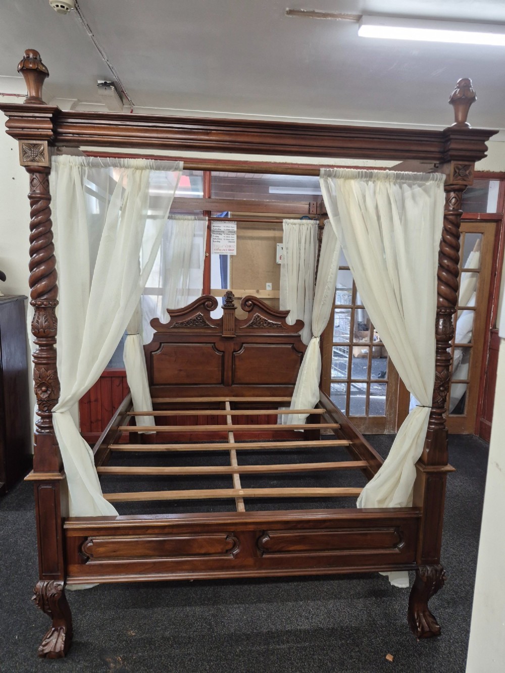 A dark hardwood queen-size four-poster bed frame featuring turned posts, a detailed carved headboard, and draped cream fabric. View XIII