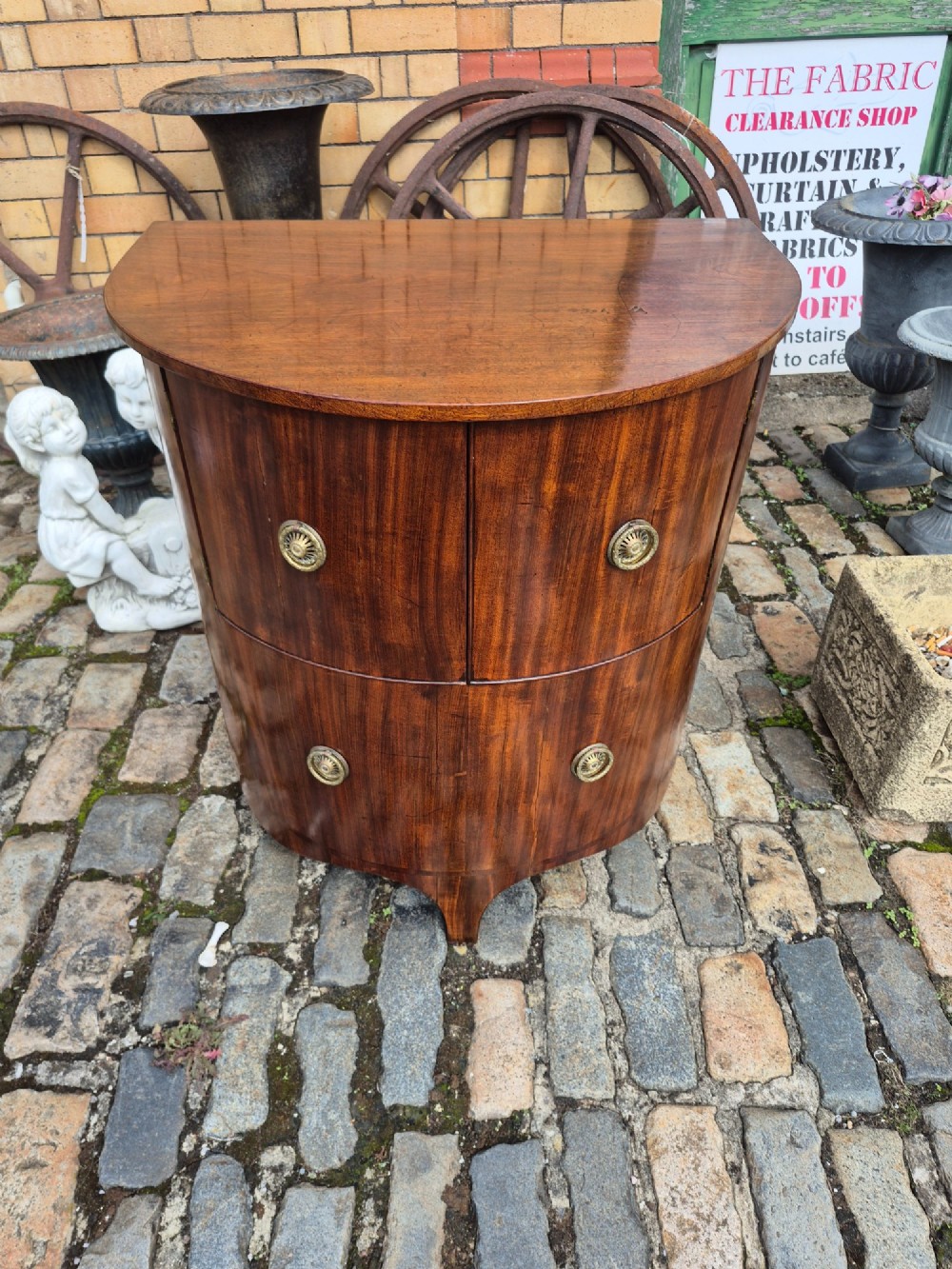 A small semi-circular mahogany cocktail cabinet featuring flame veneer panels and circular brass patera handles.