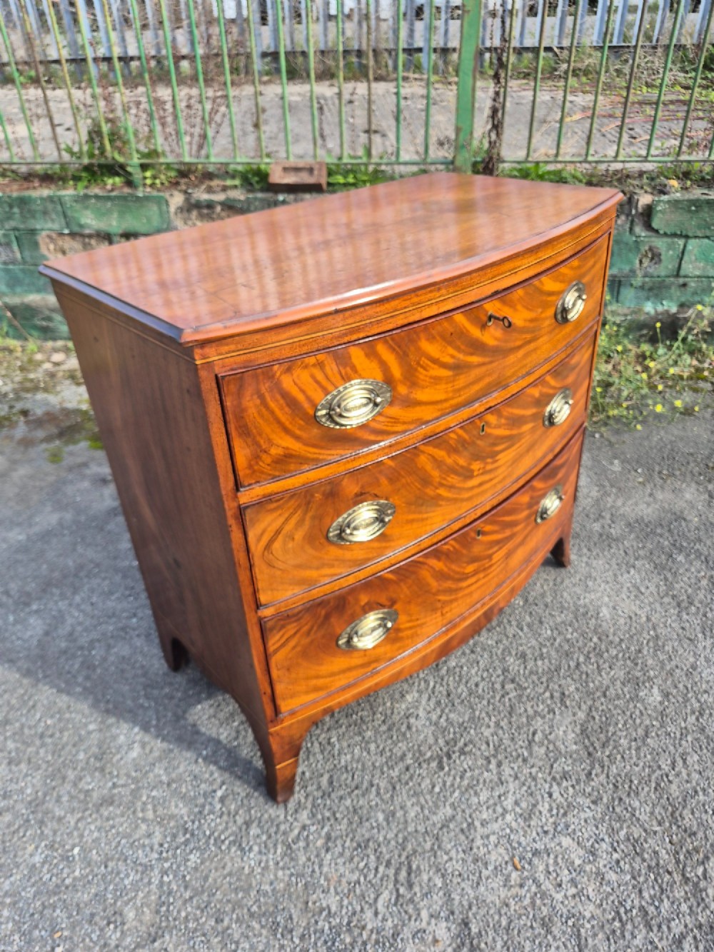 A Regency period bowfront chest of drawers crafted from flame mahogany veneer with three drawers and brass oval handles. View III