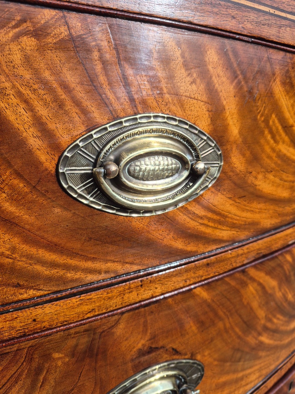 A Regency period bowfront chest of drawers crafted from flame mahogany veneer with three drawers and brass oval handles. View V