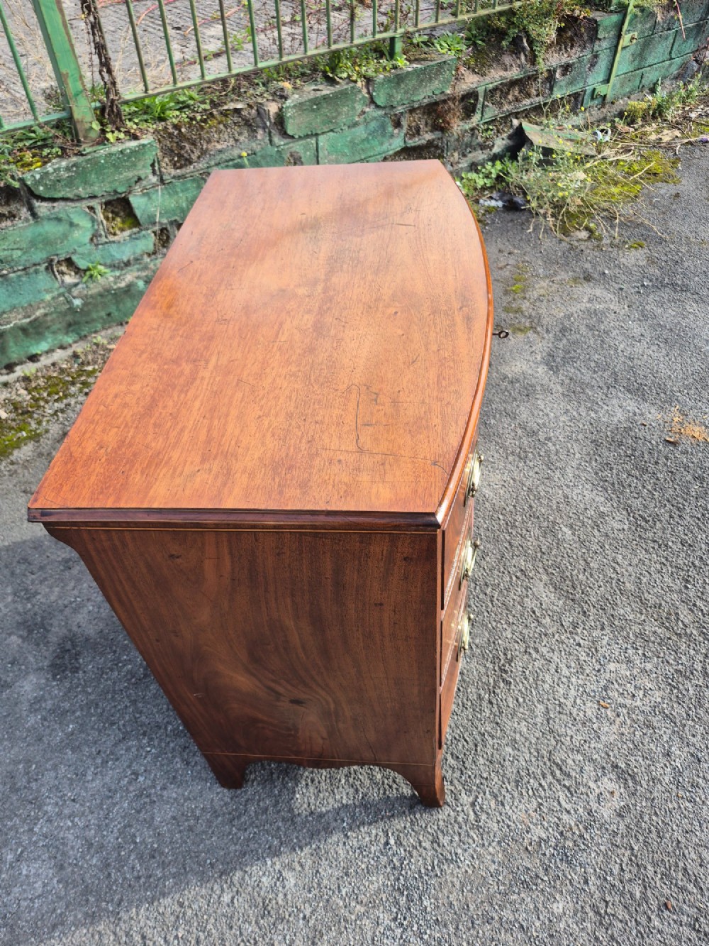 A Regency period bowfront chest of drawers crafted from flame mahogany veneer with three drawers and brass oval handles. View VI