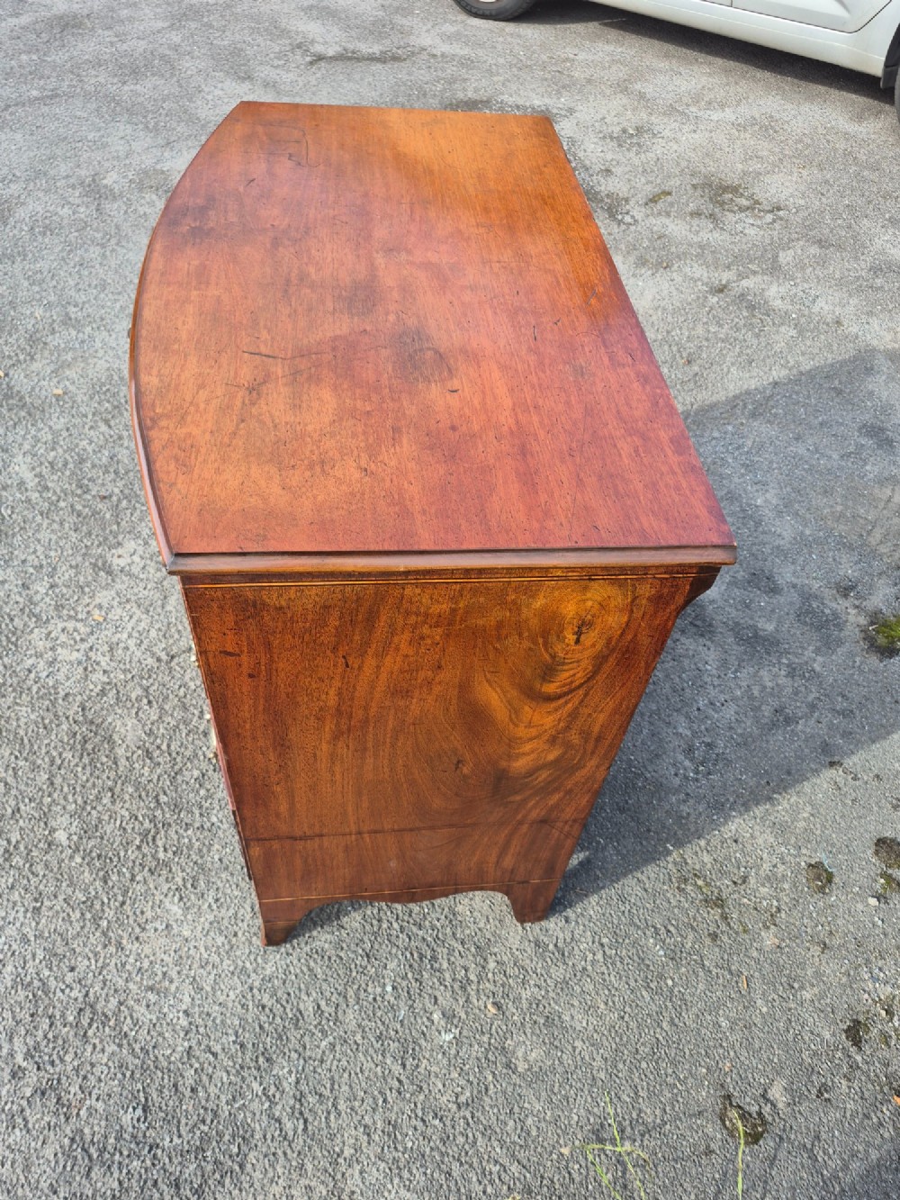 A Regency period bowfront chest of drawers crafted from flame mahogany veneer with three drawers and brass oval handles. View VII